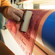 Load image into Gallery viewer, Person applying a white strip to a red and blue cylindrical object with a textured surface.
